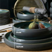 Stilvolles Tafelservice in Grün mit verschiedenen Tellergrößen, präsentiert in einer seitlichen Perspektive. Enthält Feigen als Dekoration.