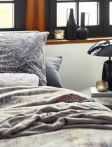 Gemütliche Bettwäsche in neutralen Tönen mit modernem Muster, seitliche Perspektive auf ein stilvoll eingerichtetes Schlafzimmer mit Dekorationen auf der Fensterbank.