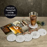Set aus sechs runden Untersetzern mit verschiedenen Gravuren, präsentiert mit einem Glas auf einem Untersetzer und einem Rezeptheft im Hintergrund. Perspektive von oben.