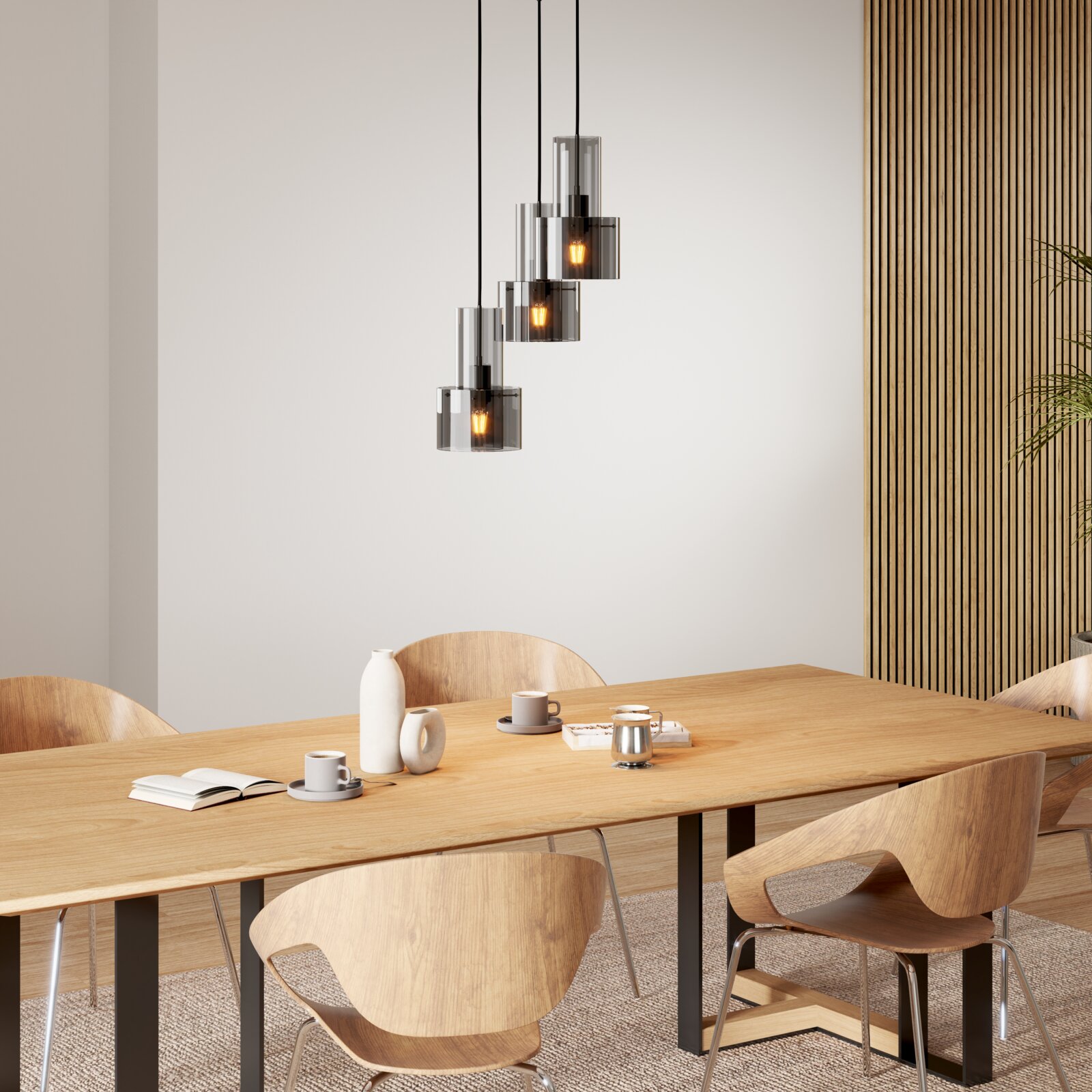 Moderne dreiflammige Pendelleuchte mit rauchgrauen Glaszylindern und warm leuchtenden Glühbirnen über einem Holzesstisch, frontale Perspektive leicht von unten