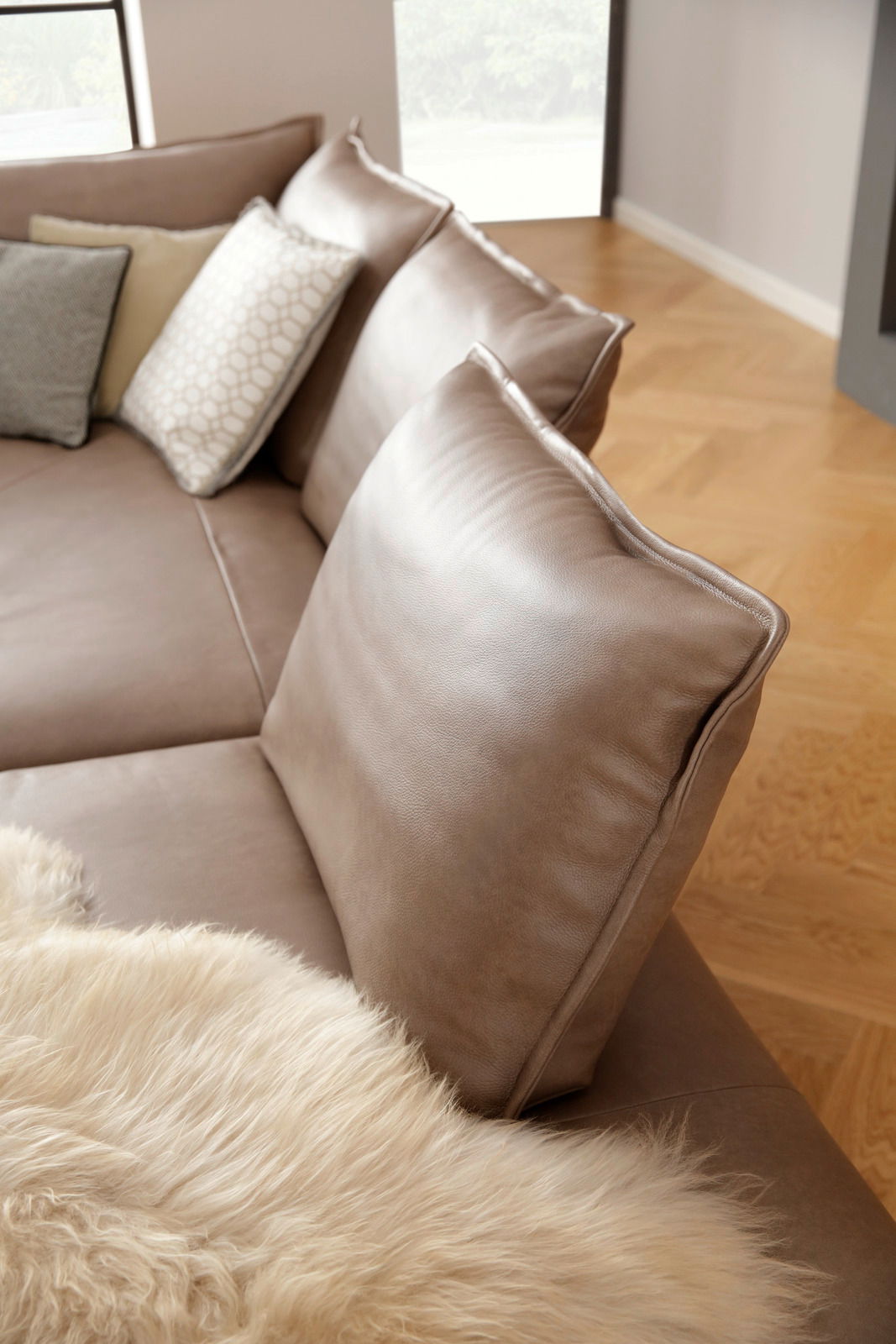 Nahaufnahme einer eleganten Polsterrundecke in Lederoptik mit mehreren Kissen und einem weichen Fellüberwurf, seitliche Perspektive.