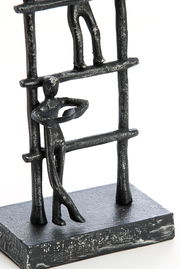 Metallische Skulptur mit zwei stilisierten Figuren auf einer Leiter, seitliche Perspektive