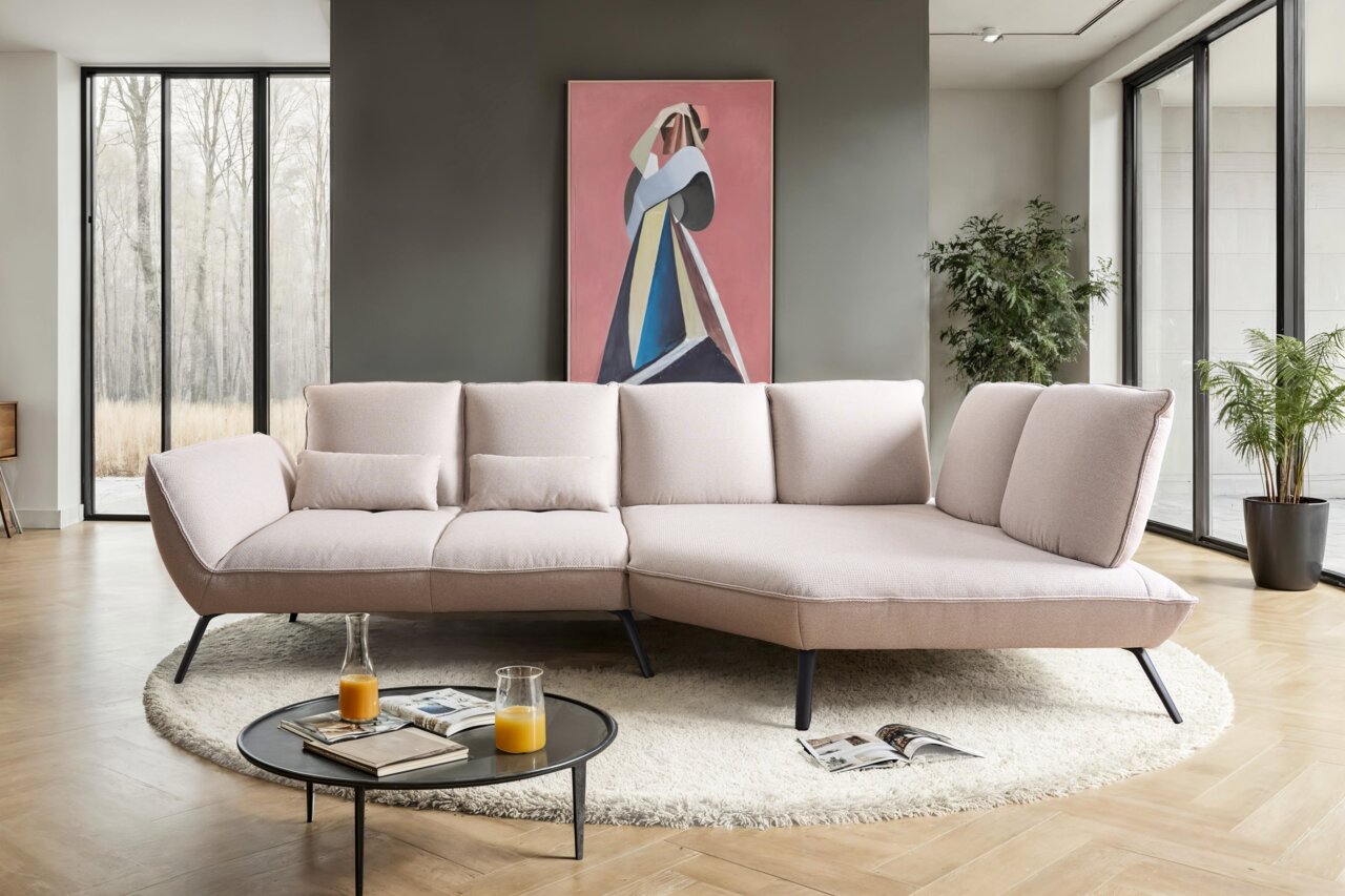 Moderne Longchairkombination in einem stilvollen Wohnzimmer, frontal von vorne fotografiert. Das Sofa hat eine helle Polsterung und steht auf einem runden Teppich, umgeben von großen Fenstern und Pflanzen.