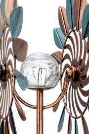 Close-up van een decoratieve zonne-lamp met bronskleurige en blauwe metalen blaadjes en een glazen bol in het midden.