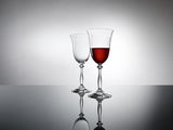 Zwei elegante Weingläser auf einer reflektierenden Oberfläche, eines gefüllt mit Rotwein, seitliche Perspektive.
