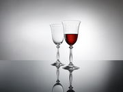 Zwei elegante Weingläser auf einer reflektierenden Oberfläche, eines gefüllt mit Rotwein, seitliche Perspektive.