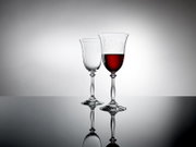 Twee elegante wijnglazen op een spiegelend oppervlak, waarvan één gevuld met rode wijn, gezien vanuit de zijkant.