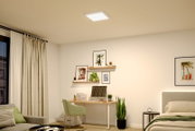 Quadratische LED-Deckenleuchte in Weiß an der Zimmerdecke, eingeschaltet, in modernem Schlafzimmer/Homeoffice – Ansicht von unten in leichter Raum-Perspektive.