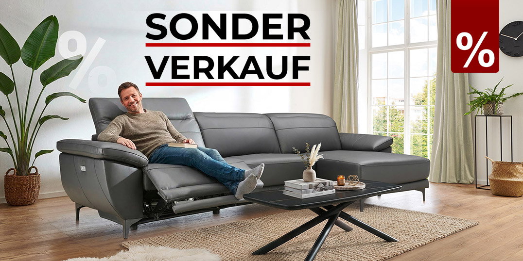 Mann entspannt auf grauem Ledersofa mit Relaxfunktion in hellem Wohnzimmer, Hinweis auf Sonderverkauf.