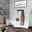Wandgarderobe aus Holz mit mehreren Haken, an der eine braune Jacke und eine schwarze Tasche hängen, in einem modernen Schlafzimmer mit Betonwänden und minimalistischer Dekoration. Perspektive: seitlich.