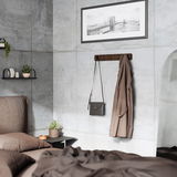 Wandgarderobe aus Holz mit mehreren Haken, an der eine braune Jacke und eine schwarze Tasche hängen, in einem modernen Schlafzimmer mit Betonwänden und minimalistischer Dekoration. Perspektive: seitlich.