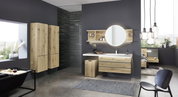 Moderne Badezimmeransicht mit Holzschränken, rundem Spiegel und Wäschebox auf Rollen, seitliche Perspektive.