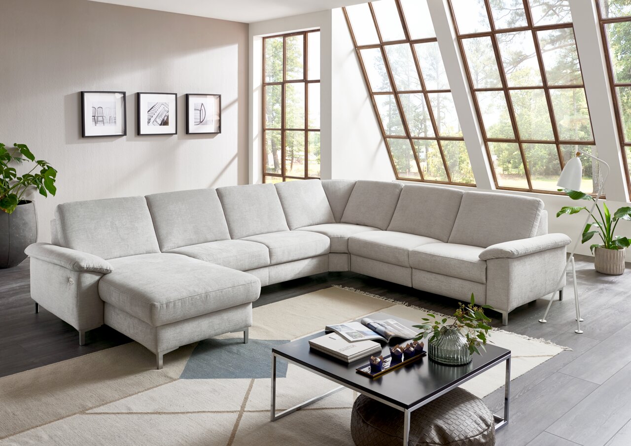 Helle Polsterrundecke in einem modernen Wohnzimmer mit großen Fenstern, aus der Perspektive von vorne links betrachtet.