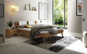 Modernes Schlafzimmer mit einem Kopfteil aus Holz und Metall, seitliche Perspektive. Das Bett ist mit weißen und grauen Kissen sowie einer grünen Decke dekoriert. Ein Nachttisch aus Holz steht daneben, und große Fenster lassen viel Tageslicht herein.