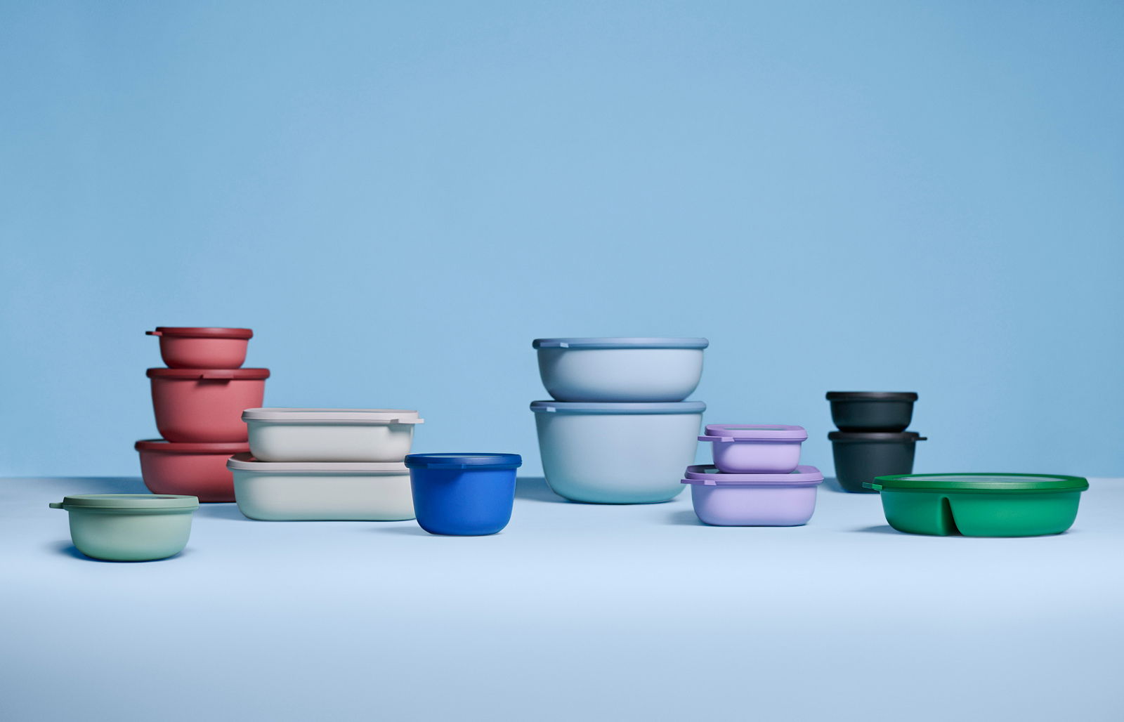 Mepal Bento Bowl Vivid mauve CIRQULA Verschiedene bunte Bento-Schalen in verschiedenen Größen und Farben, darunter rosa, blau, grün und lila, auf einer hellblauen Oberfläche. Die Schalen sind aus Kunststoff und haben runde und rechteckige Formen. Perspektive von vorne.