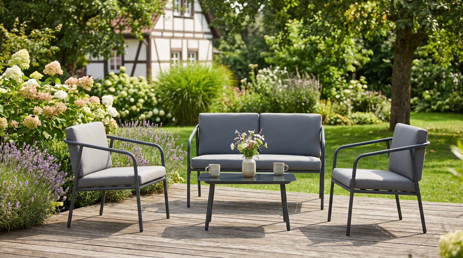 Modernes Outdoor-Lounge-Set mit grauen Polstern und schwarzem Metallgestell (2 Sessel, 2-Sitzer-Sofa und niedriger Tisch) auf Holzterrasse im Garten, frontal in leichter Schrägansicht aufgenommen