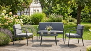 Modernes Outdoor-Lounge-Set mit grauen Polstern und schwarzem Metallgestell (2 Sessel, 2-Sitzer-Sofa und niedriger Tisch) auf Holzterrasse im Garten, frontal in leichter Schrägansicht aufgenommen
