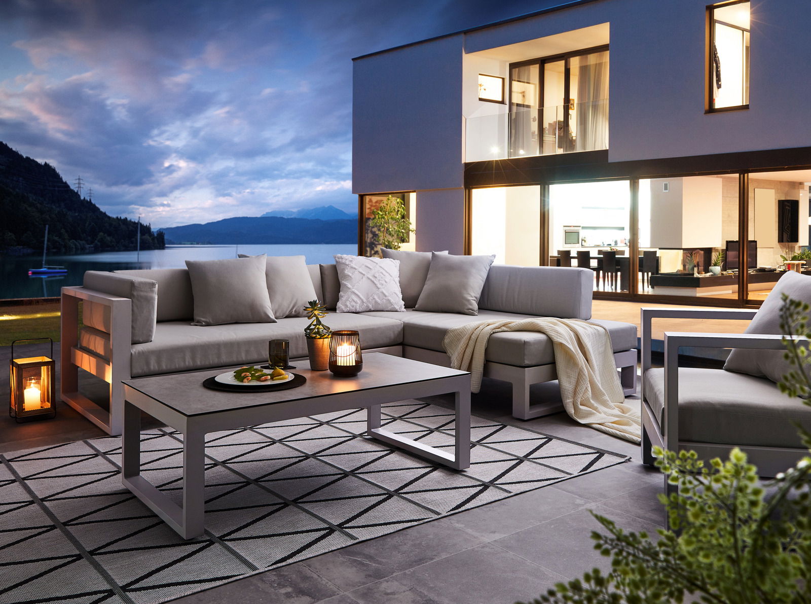 Modernes Lounge-Set auf einer Terrasse mit Blick auf einen See bei Dämmerung, seitliche Perspektive.