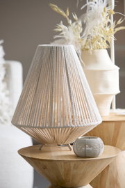 Tafellamp met een gevlochten lampenkap van licht materiaal, staande op een houten tafel, gezien vanaf de zijkant.