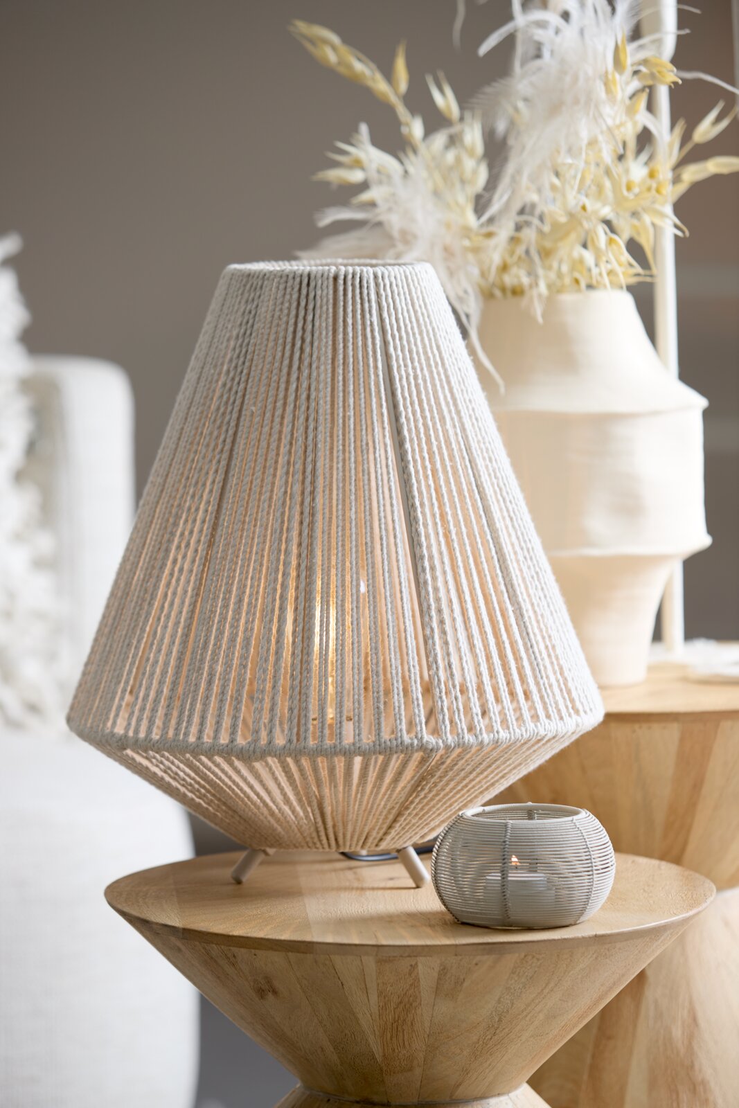 Tafellamp met een gevlochten lampenkap van licht materiaal, staande op een houten tafel, gezien vanaf de zijkant.