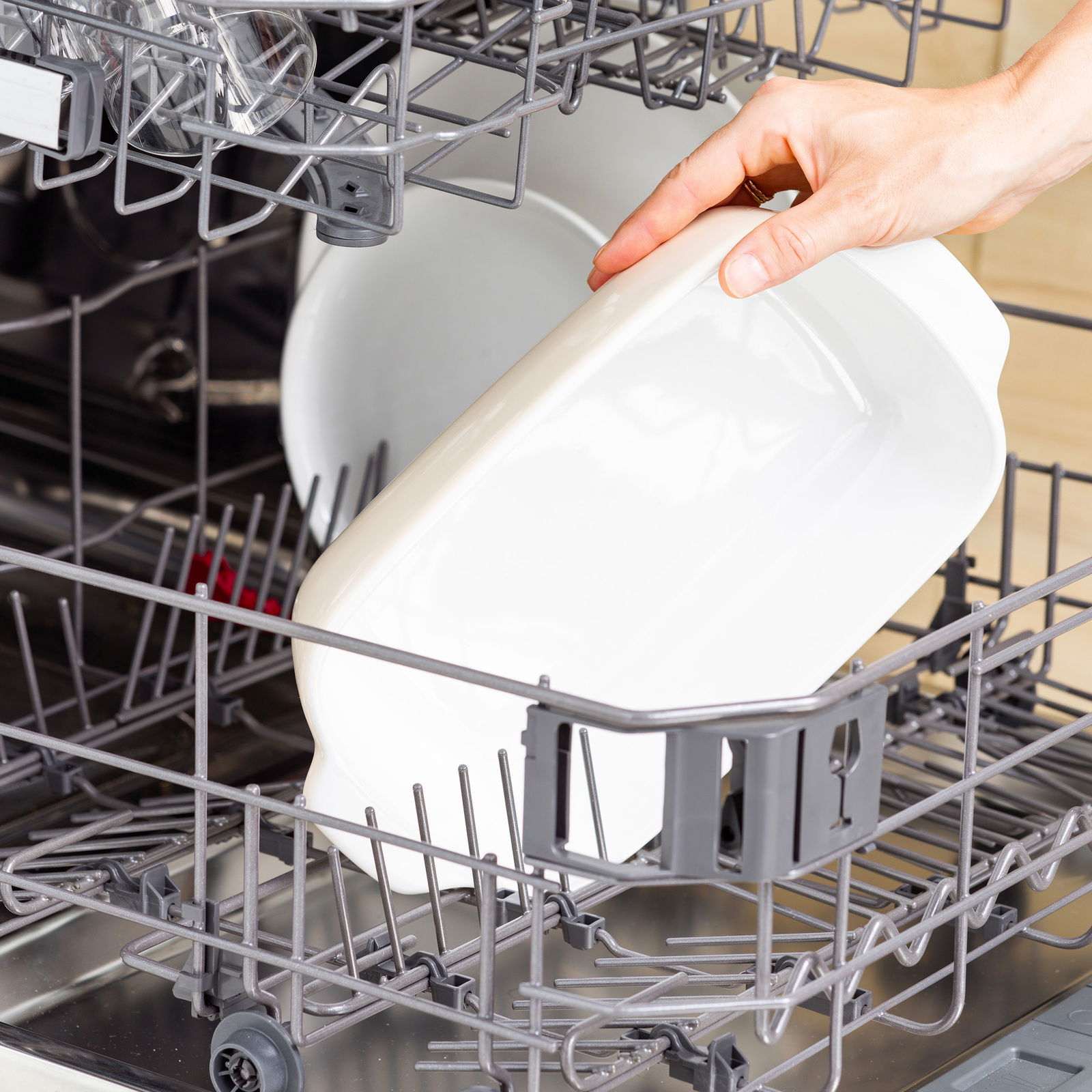 Weiße Auflaufform mit Deckel wird in eine Spülmaschine eingeräumt, seitliche Perspektive.