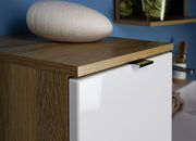 Nahaufnahme eines Schranks mit Holzoberfläche und weißer Tür, darauf liegt eine ovale, weiße Dekoration. Perspektive von schräg oben.