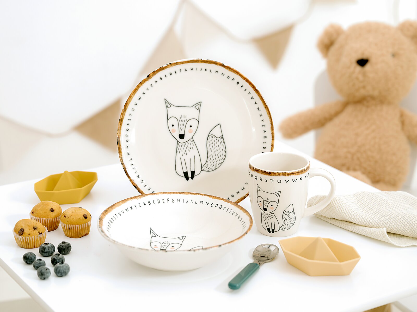 Kinder-Geschirrset aus Teller, Schale und Henkelbecher mit Fuchs- und Alphabetmotiv, aus schräger Vorderansicht auf einem gedeckten Tisch präsentiert