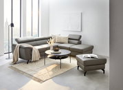 Moderner Wohnraum mit grauem Ecksofa, rundem Couchtisch und Hocker mit Stauraum, seitliche Perspektive.