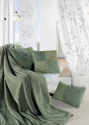 Gemütliche Wohnzimmerszene mit grünen Kissen und Decke auf einem Sofa, umgeben von weißen Vorhängen mit Pflanzenmuster. Perspektive von vorne.