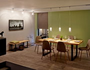 Esszimmer mit modernem Schienenpendel Arido II, das über einem Esstisch mit sechs Stühlen hängt. Die Perspektive zeigt den Raum von der Seite, mit einem grünen Akzent an der Wand.