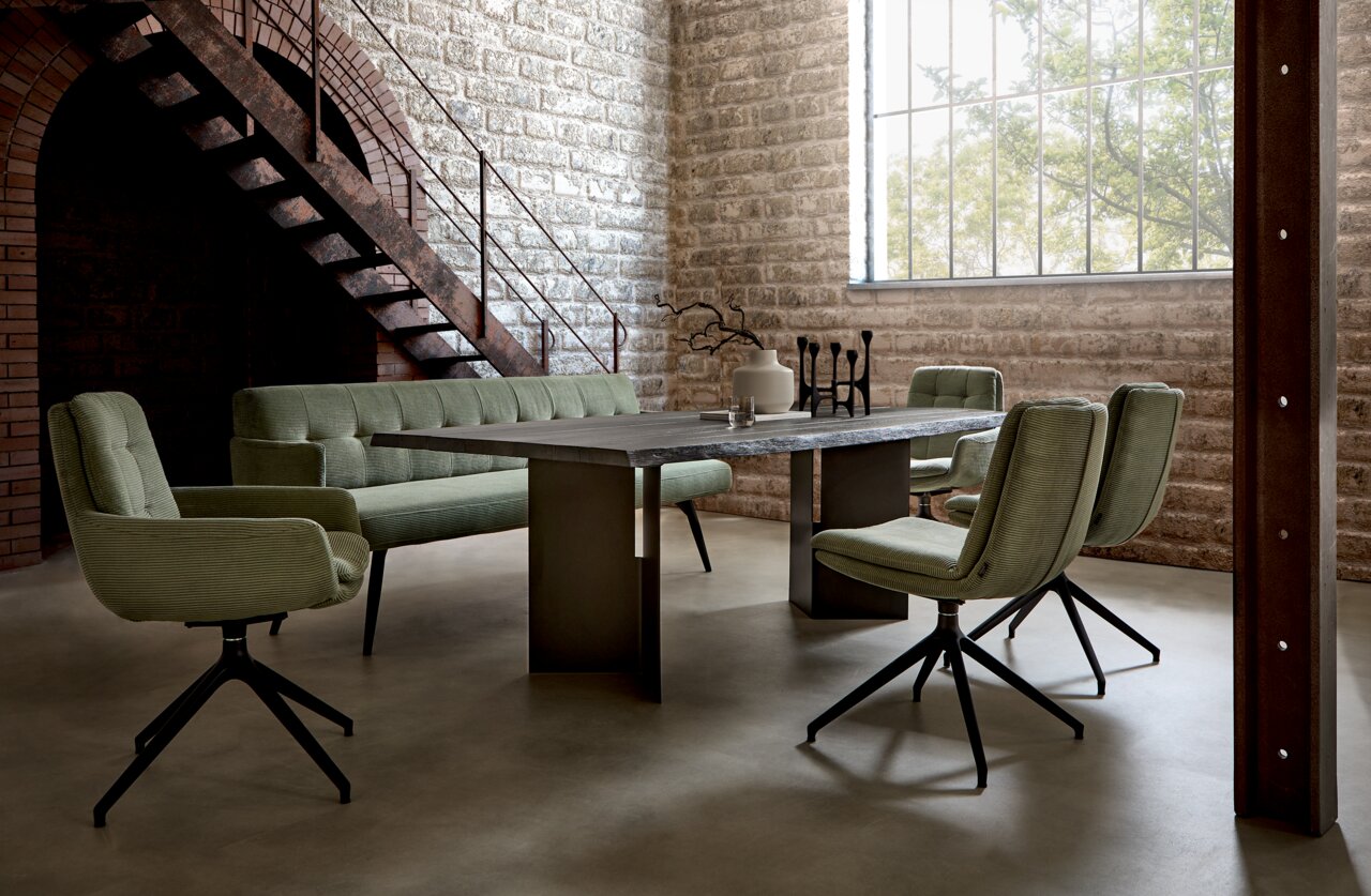 Moderner Esstisch in einem industriellen Loft mit grünen Stühlen und Sofa, seitliche Perspektive