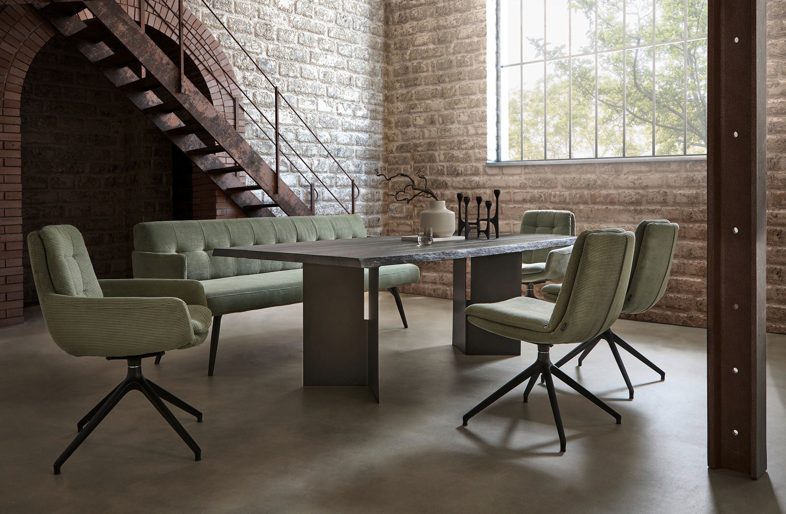 Moderner Esstisch in einem industriellen Loft mit grünen Stühlen und Sofa, seitliche Perspektive