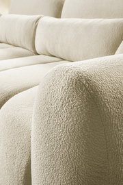 Nahaufnahme eines cremefarbenen Bouclé-Stoffsofas mit weich gepolsterten Sitz- und Rückenkissen, Perspektive: schräg von vorne auf die Armlehne und Sitzfläche
