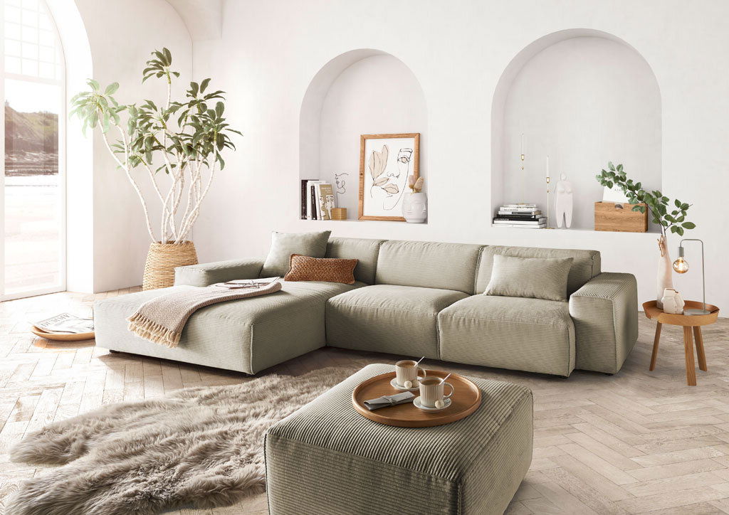 Moderne Rundecke in einem hellen Wohnzimmer mit großen Fenstern, Pflanzen und stilvollen Dekorationen, aus der Perspektive von vorne links.