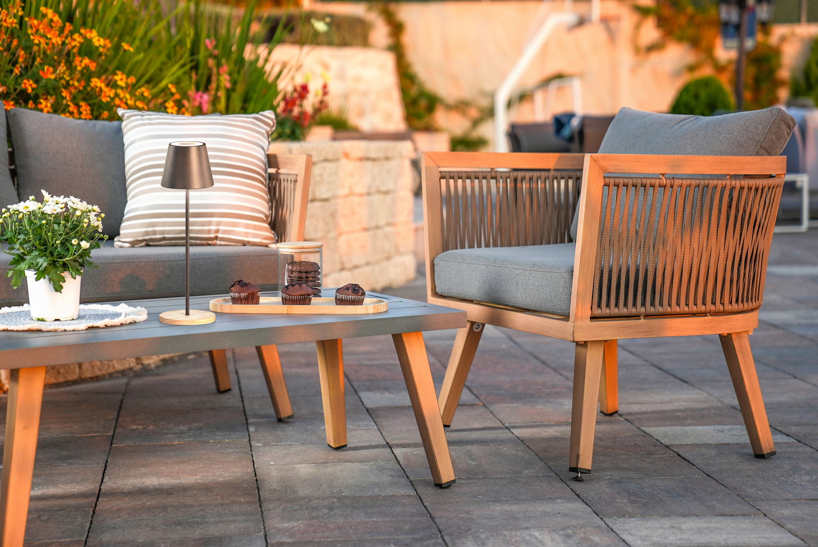 Akku-Tischleuchte COSENZA auf einem Terrassentisch, umgeben von Gartenmöbeln und Pflanzen, seitliche Perspektive.