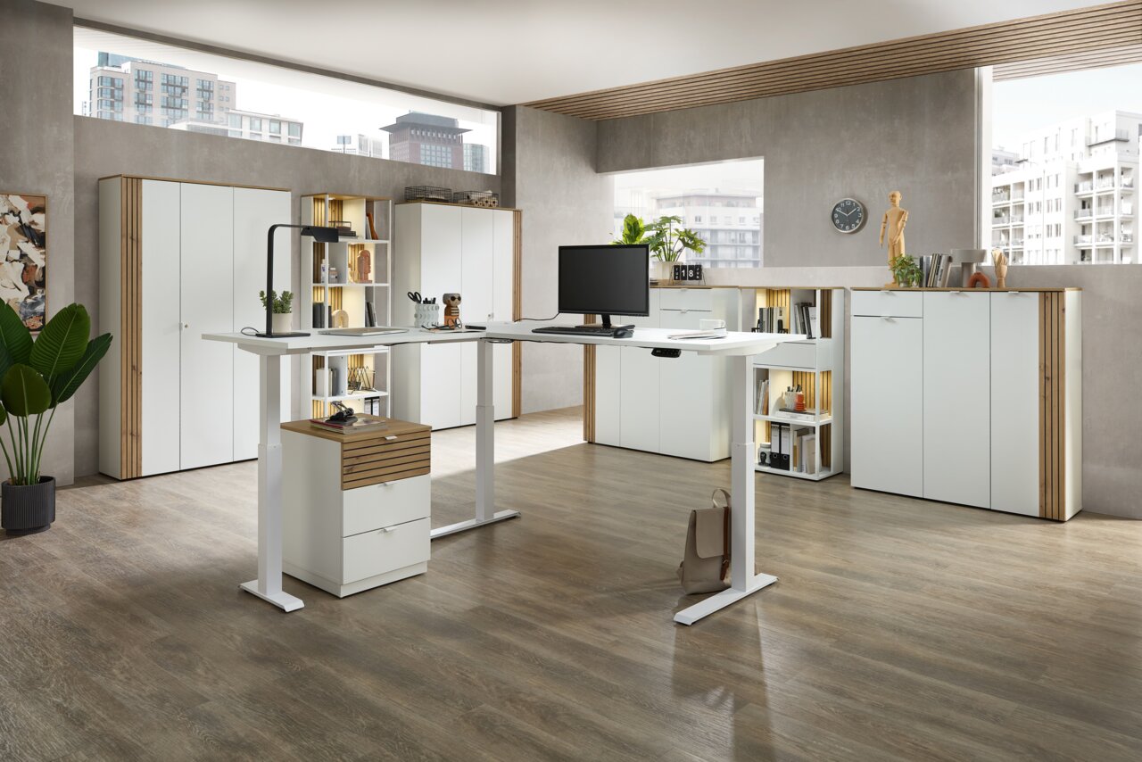 Een moderne kantooromgeving met een in hoogte verstelbaar hoekbureau, omringd door witte kantoorkasten en rekken, gezien vanuit een open ruimte met grote ramen.