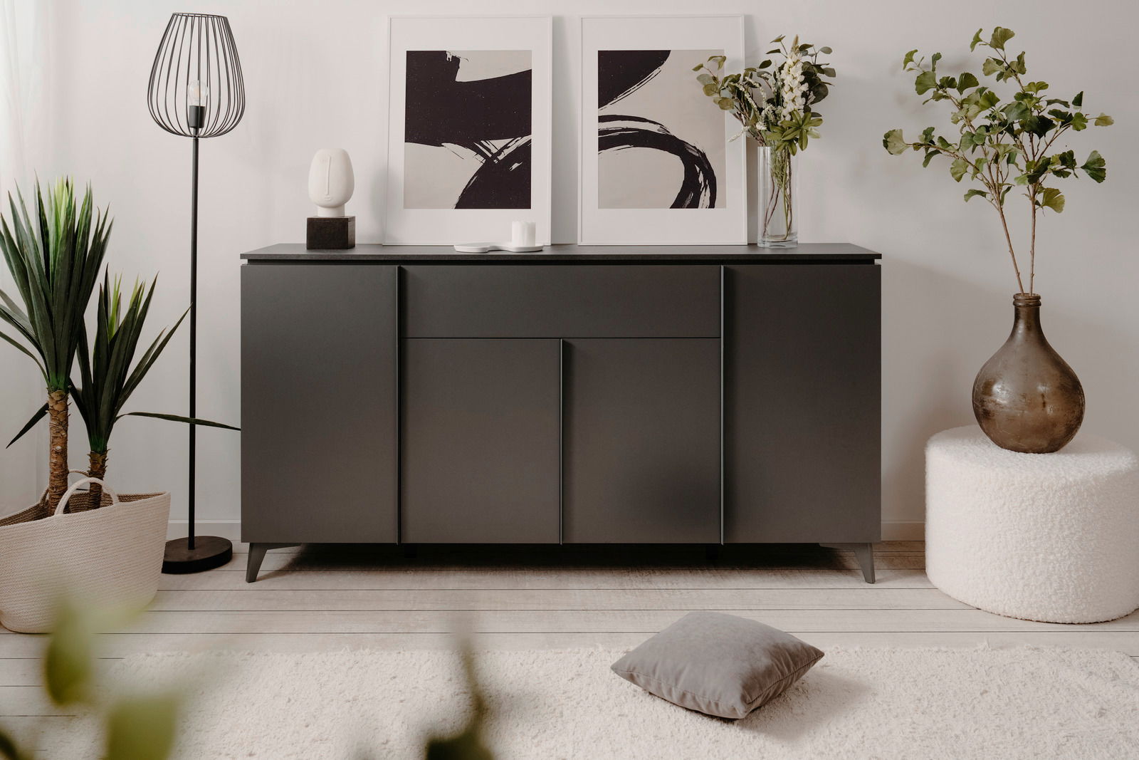Modernes Sideboard in dunklem Grau, frontal fotografiert, dekoriert mit Kunstwerken, Pflanzen und einer Lampe.
