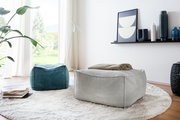 Zwei quadratische Hocker in einem modernen Wohnzimmer, einer in Grau und einer in Blau, auf einem runden Teppich vor einem großen Fenster. Perspektive von schräg oben.
