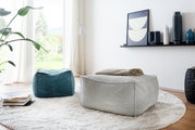 Twee vierkante poefs in een moderne woonkamer, één in grijs en één in blauw, op een rond tapijt voor een groot raam. Aanzicht van schuin bovenaf.