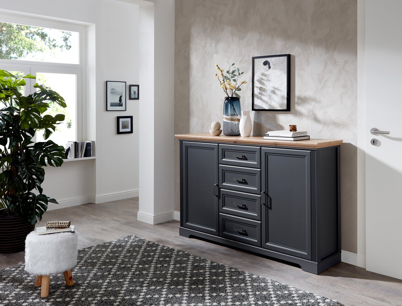 Dunkelgraues Sideboard mit Holzplatte, dekoriert mit Vasen und Büchern, in einem modernen Wohnzimmer. Perspektive von vorne.