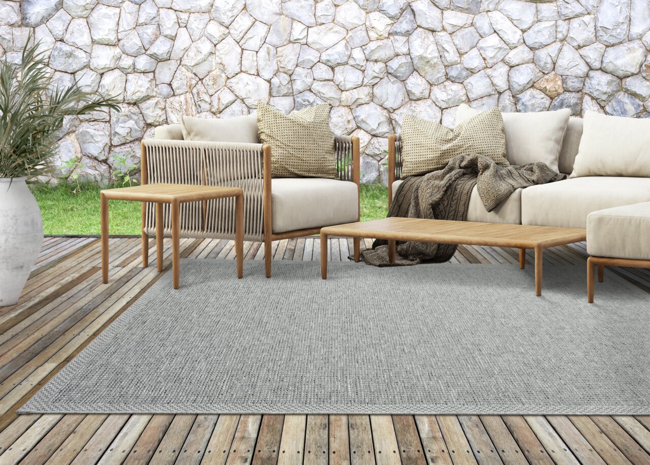 Moderner Outdoor-Bereich mit grauem Teppich, Holzmöbeln und bequemen Kissen, von vorne betrachtet.