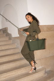 Frau in einem olivgrünen Overall, die eine olivgrüne Tragetasche auf einer Treppe trägt, seitliche Perspektive.