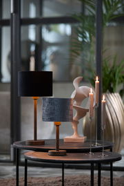 Zwei stilvolle Tischlampen mit Holzfuß und unterschiedlichen Lampenschirmen, eine in Schwarz und die andere mit Krokodilledermuster, auf runden Tischen in einem modernen Interieur. Seitliche Perspektive.