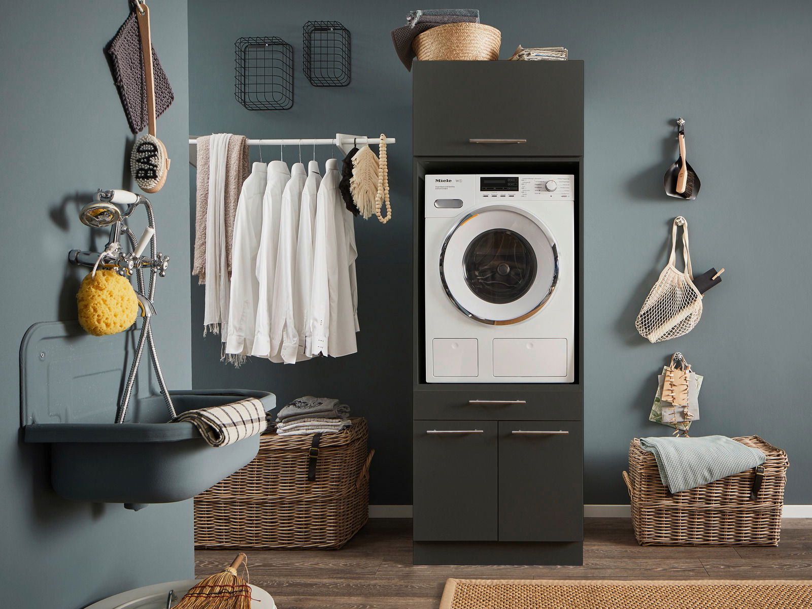 Hauswirtschaftsraum mit Waschmaschine in einem dunklen Schrank, umgeben von Körben und einem Waschbecken. Frontalansicht.