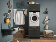 Hauswirtschaftsraum mit Waschmaschine in einem dunklen Schrank, umgeben von Körben und einem Waschbecken. Frontalansicht.