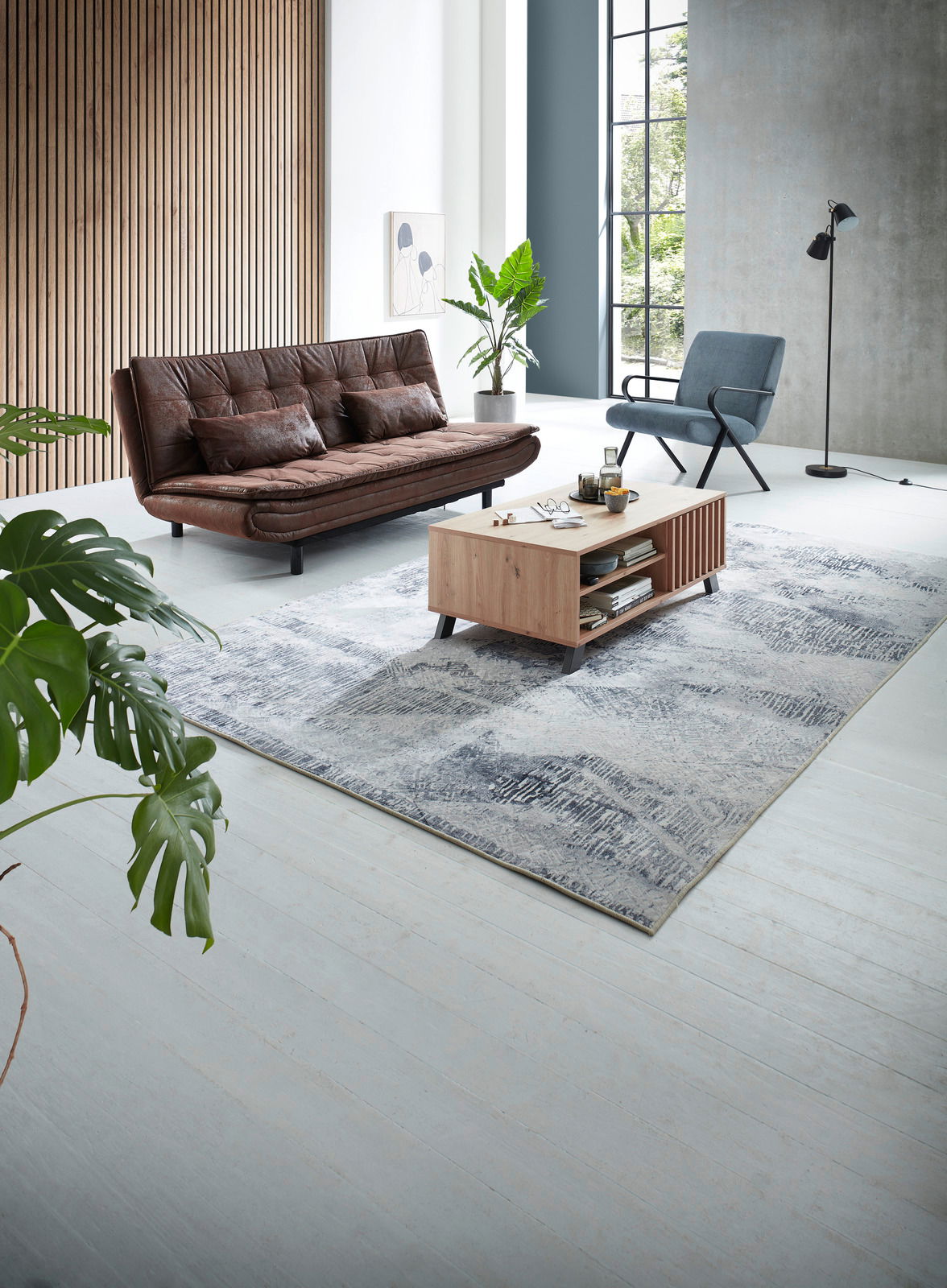 Moderner Wohnraum mit einem braunen Ledersessel, einem blauen Stuhl und einem Holzcouchtisch auf einem gemusterten Teppich. Perspektive von oben.