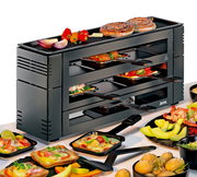 Perspektive von schräg vorne: Ein schwarzes Pizza-Raclette-Gerät mit mehreren Ebenen, auf denen Pfännchen mit verschiedenen Zutaten wie Gemüse und Käse zu sehen sind. Auf der oberen Grillfläche liegen Würstchen und Gemüse.