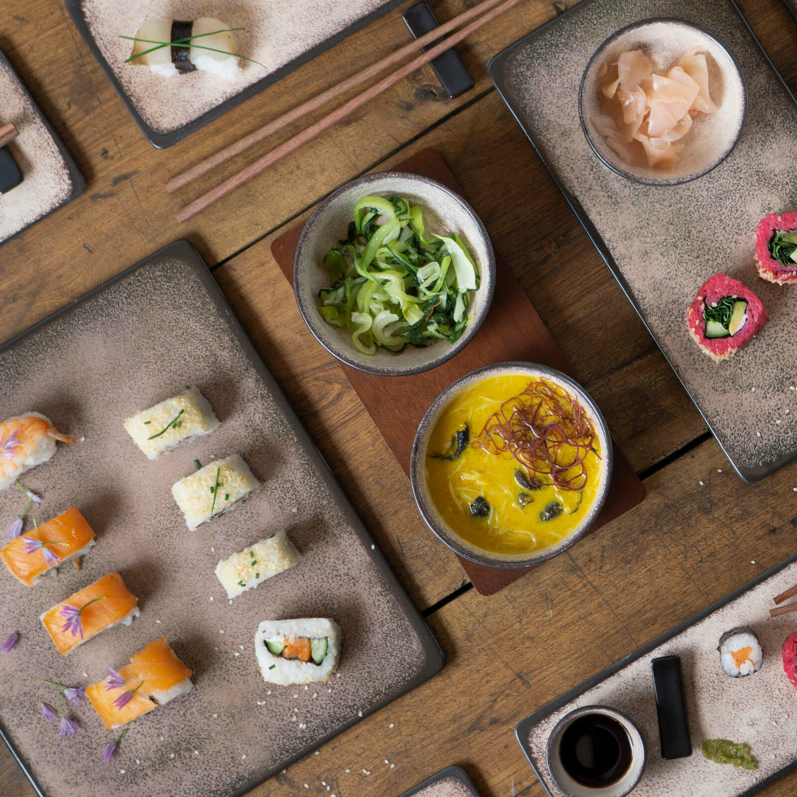 Vogelperspektive auf ein 29-teiliges Sushi-Set in Beige mit verschiedenen Sushi-Varianten und Beilagen auf einem Holztisch.