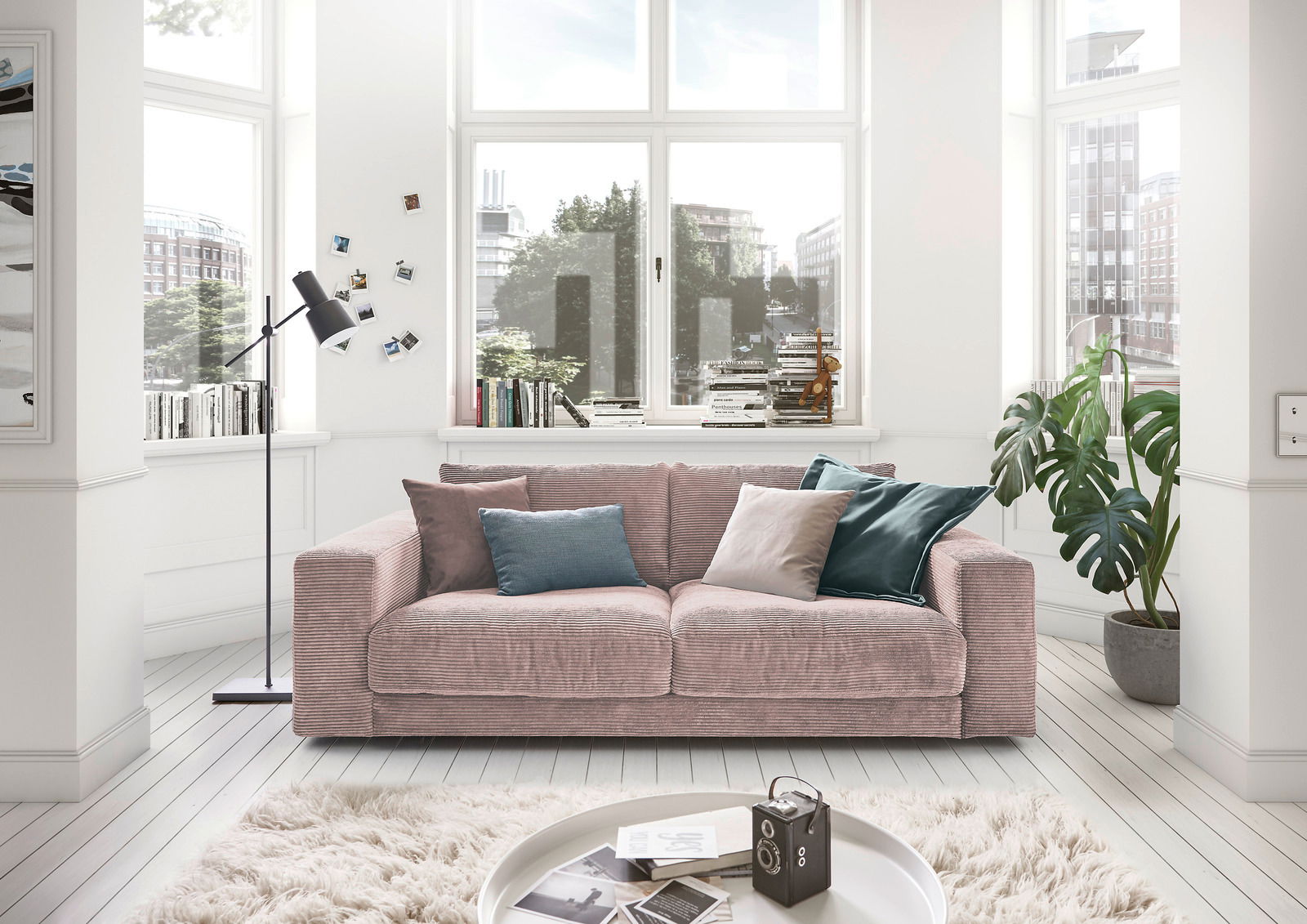 Gemütliches 2-Sitzer-Sofa in einem hellen Wohnzimmer mit großen Fenstern, dekoriert mit bunten Kissen, aus der Frontalperspektive.