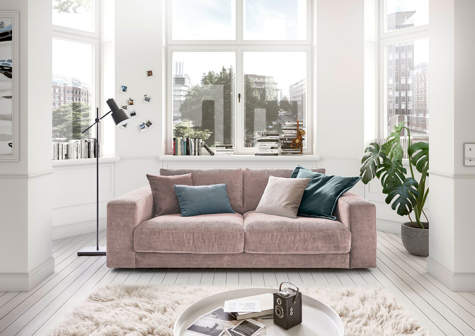 Gemütliches 2-Sitzer-Sofa in einem hellen Wohnzimmer mit großen Fenstern, dekoriert mit bunten Kissen, aus der Frontalperspektive.